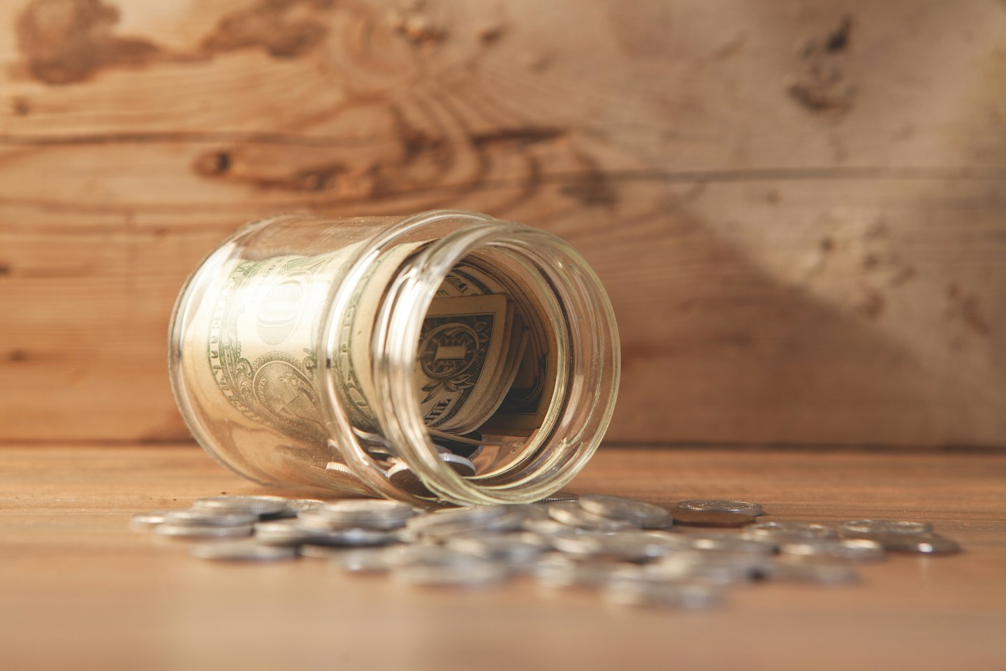 Gerollte Dollarnoten in einem Glasgefäß, umgeben von Münzen.